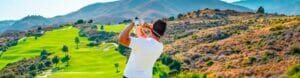 ViVi Real Estate: Ein Mann genießt einen Golfurlaub an der Costa del Sol und hält einen Golfschläger vor einem majestätischen Berg.