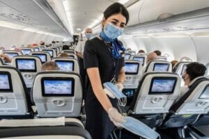 ViVi Real Estate: Een stewardess die een gezichtsmasker draagt, zorgt voor veilig vliegen tijdens coronatijden in een vliegtuig.