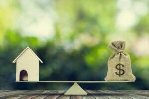 ViVi Real Estate: Dom i worek pieniędzy na skali bilansowej, symbolizującej wagę bogactwa w stosunku do majątku.